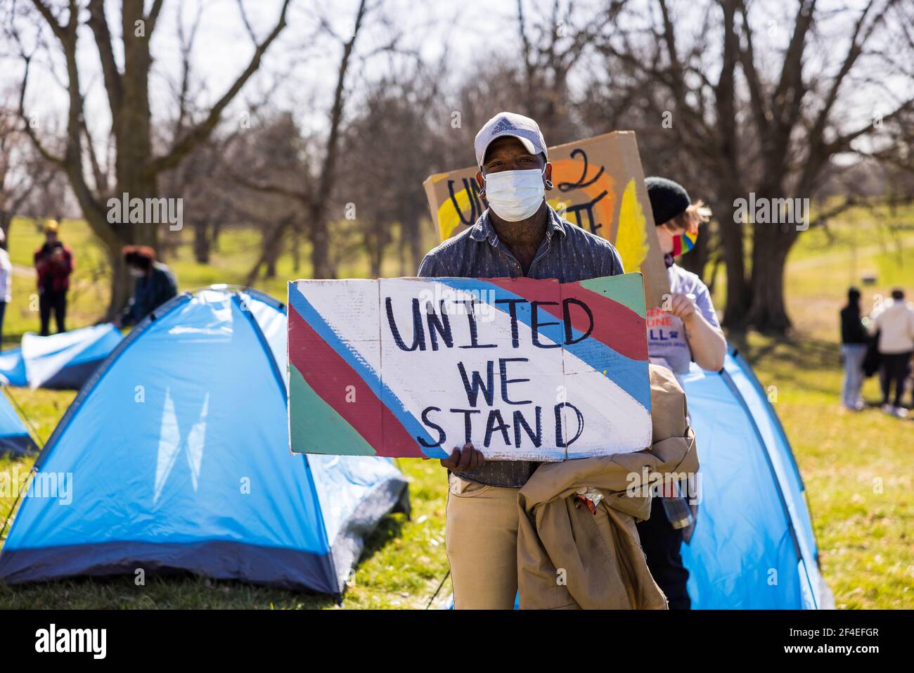 Ein Protestler hält ein Protestschild "United We Stand" . Eine Koalition von Mitgliedern der Bloomington-Gemeinschaft, Aktivisten, Und Indiana University Studenten marschieren von Dunn Meadow zu Simon Skjodt Assembly Hall während der "March to End the Madness", um gegen die City of Bloomington Behandlung von unbewohnten Bewohnern Pitching Zelte auf öffentlichem Eigentum und die 10 Millionen Dollar Abfindungszahlung Indiana University muss gefeuert zu zahlen Basketballtrainer Archie Miller für Herren. Mehrere Spiele für das NCAA Basketball-Turnier wurden in der Assembly Hall gespielt, darunter das St. Bonaventure vs. LSU-Spiel Stockfoto