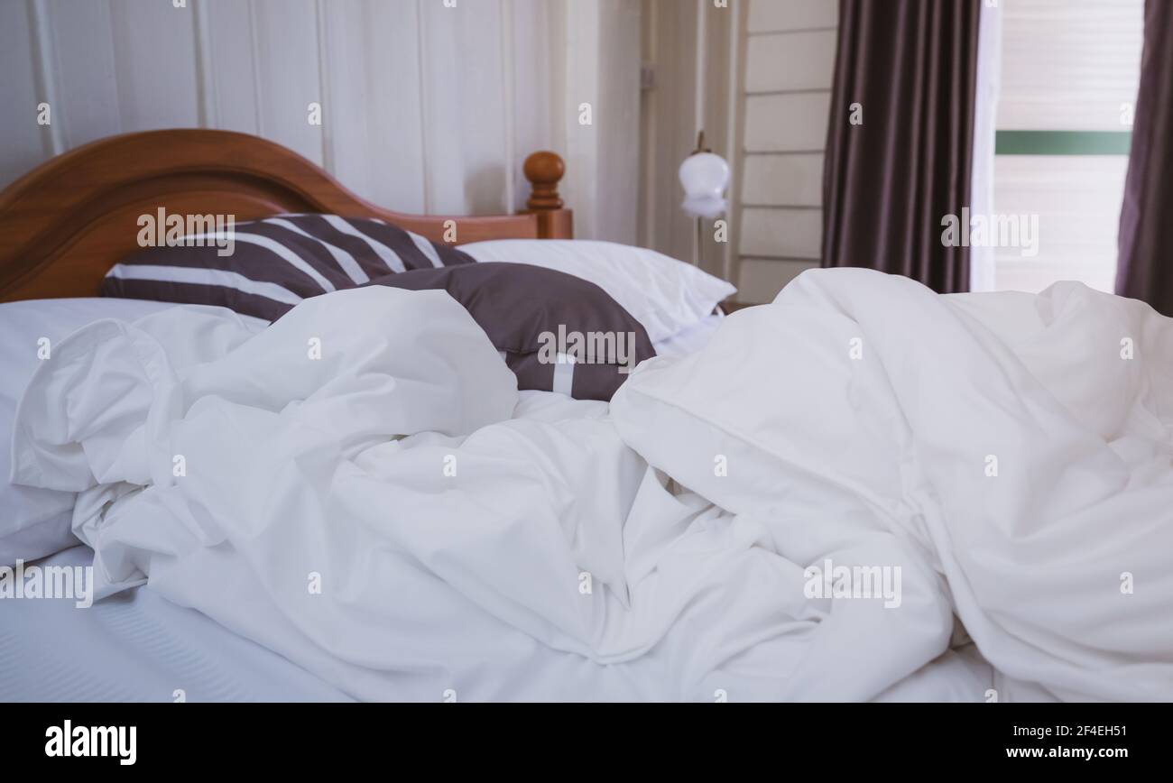 Weißes Komfortbett und weiches Kissen im Vintage-Schlafzimmer mit Fenstervorhang und Lampe. Weiße Leinendecke im Vintage-Schlafzimmer. Unordentliche weiße Decke. Stockfoto