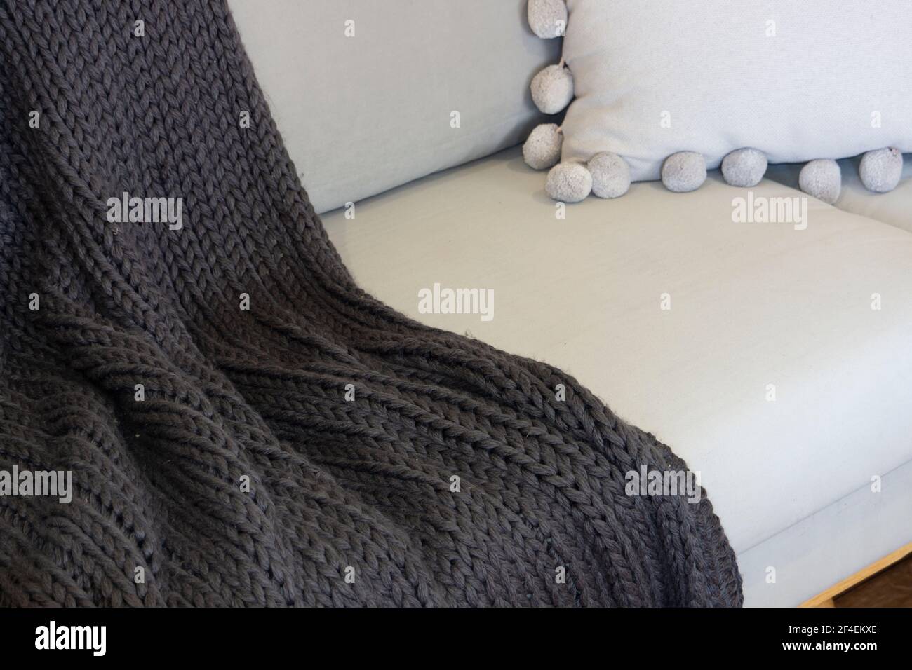 Ein luxuriöser grauer Strickteppich über dem Ende eines Sofas in neutralen Grautönen. Stockfoto
