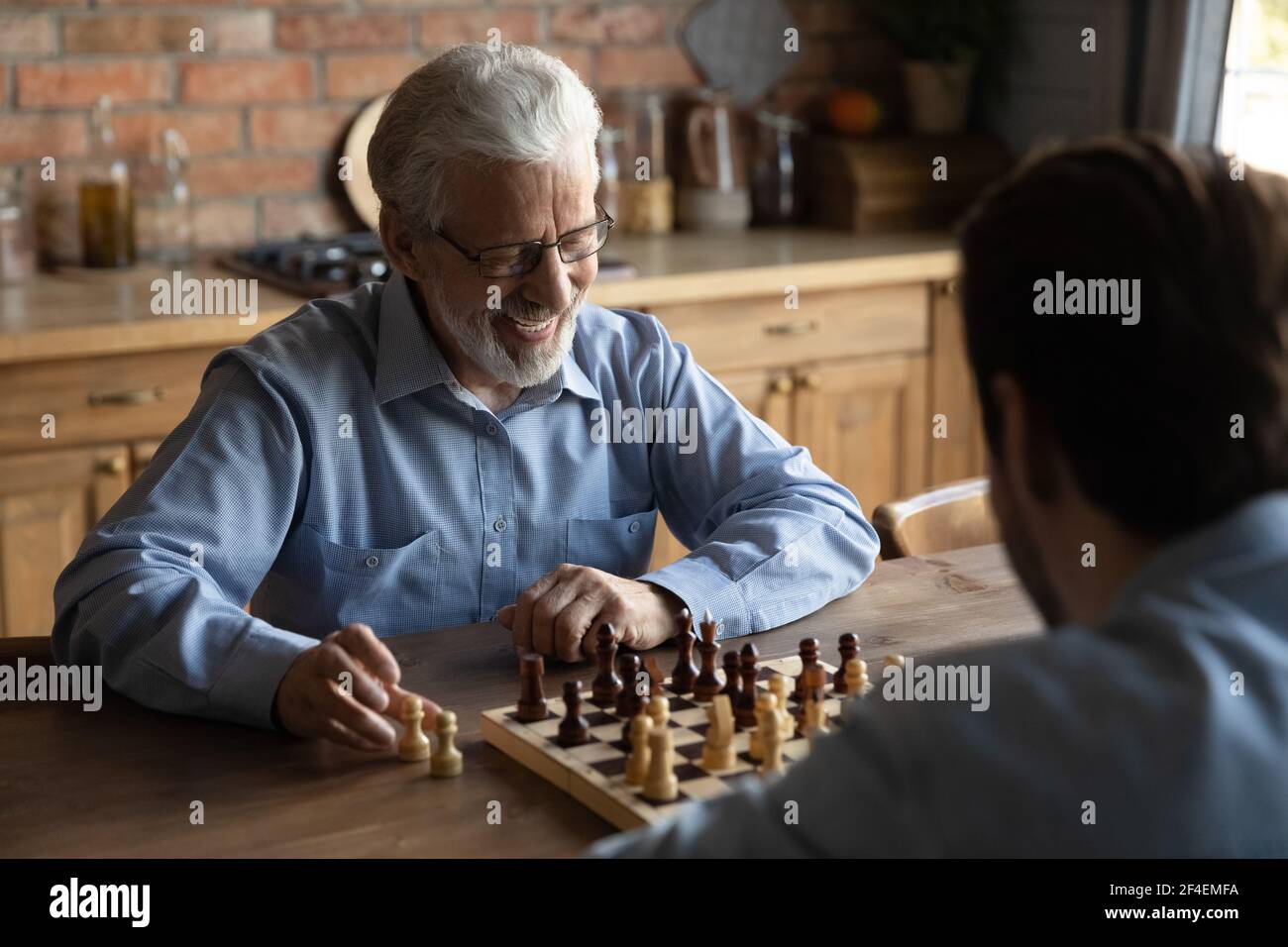 Lächelnder älterer Vater spielt Schach mit erwachsener Sohn Stockfoto