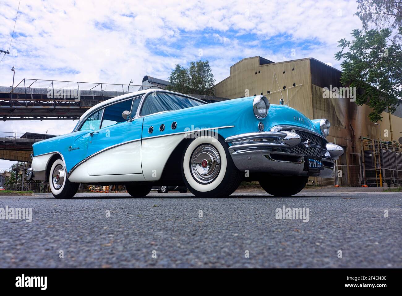 Ein tiefer Blick auf eine restaurierte klassische amerikanische Buick-Limousine aus dem Jahr 1955 in Blau und Weiß vor einem industriellen Mühlenhintergrund mit Kopierraum. Stockfoto