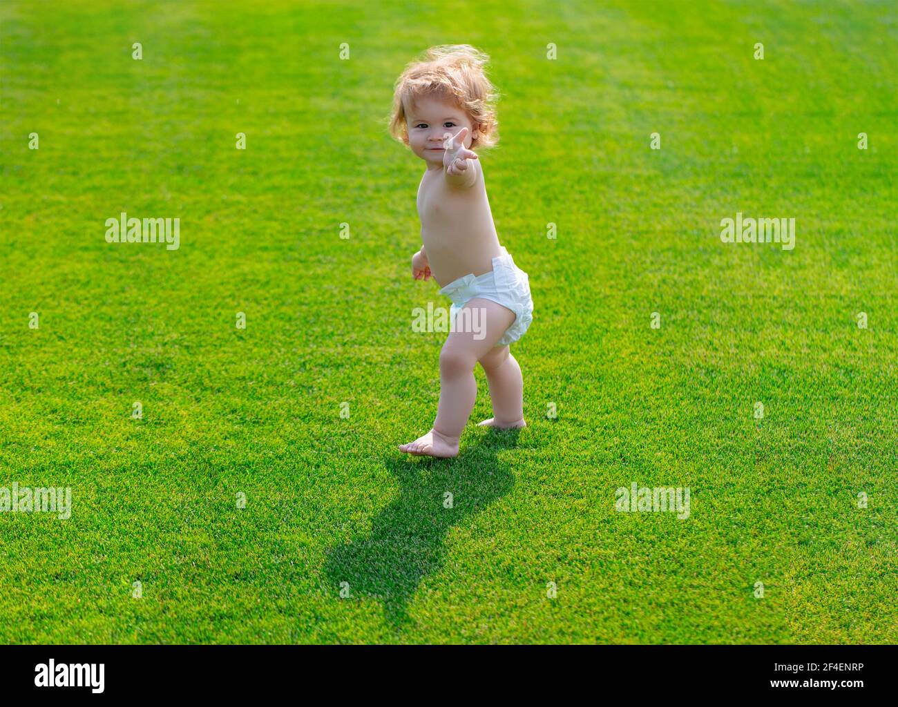 Baby Walking barfuß auf grünem Gras in sonnigen Sommerabend. Kleiner Junge, der im Sommerpark in Windelhosen spielt. Stockfoto