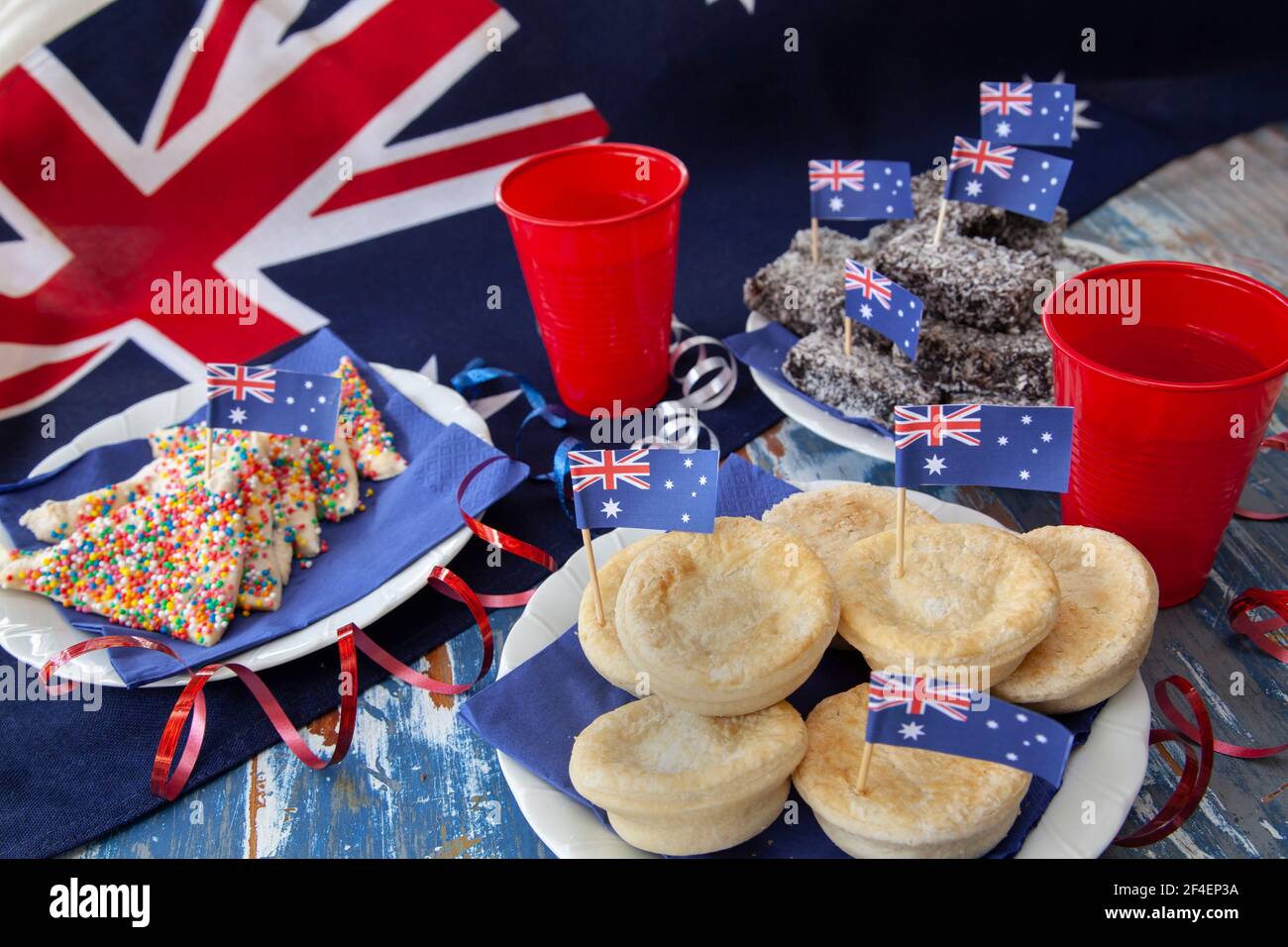 Party Food traditionell am Australia Day, dem 26th. Januar, mit Fairy Bread, Fleischpasteten und lamington Kuchen gegen eine australische Flagge gegessen. Stockfoto