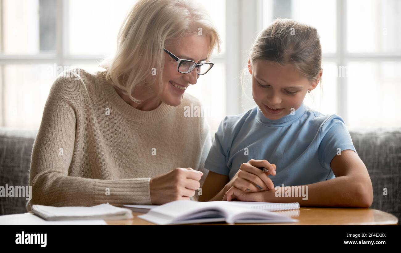 Lächelnde Großmutter und Enkelin machen gemeinsam Hausaufgaben Stockfoto