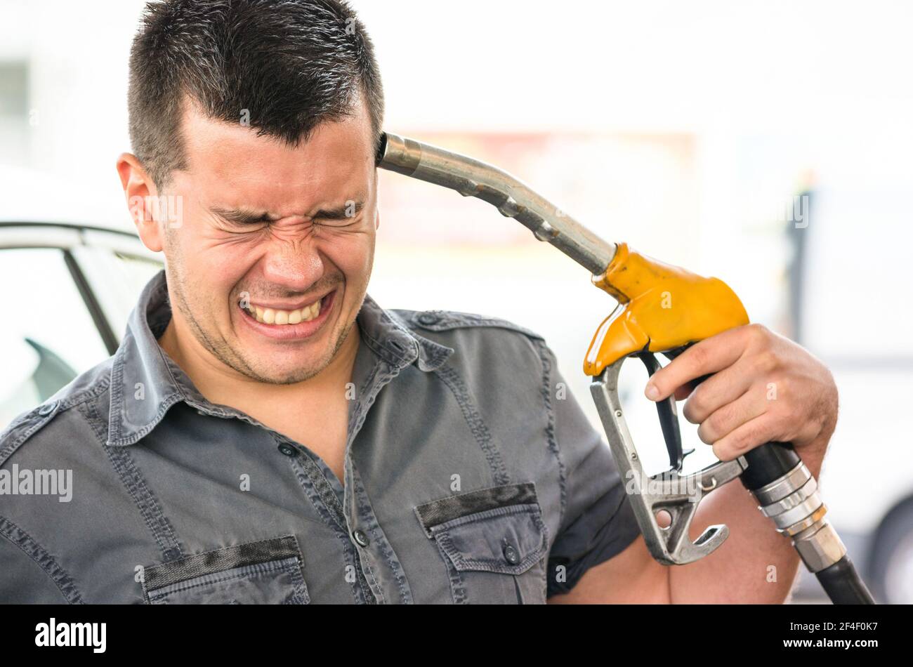 Junger Mann in Selbstmord imitiert Position an der Tankstelle - Benzin Preis steigenden Konzept mit verzweifelten Kerl zeigen Pumpe Düsen Pistole auf Kopf Stockfoto