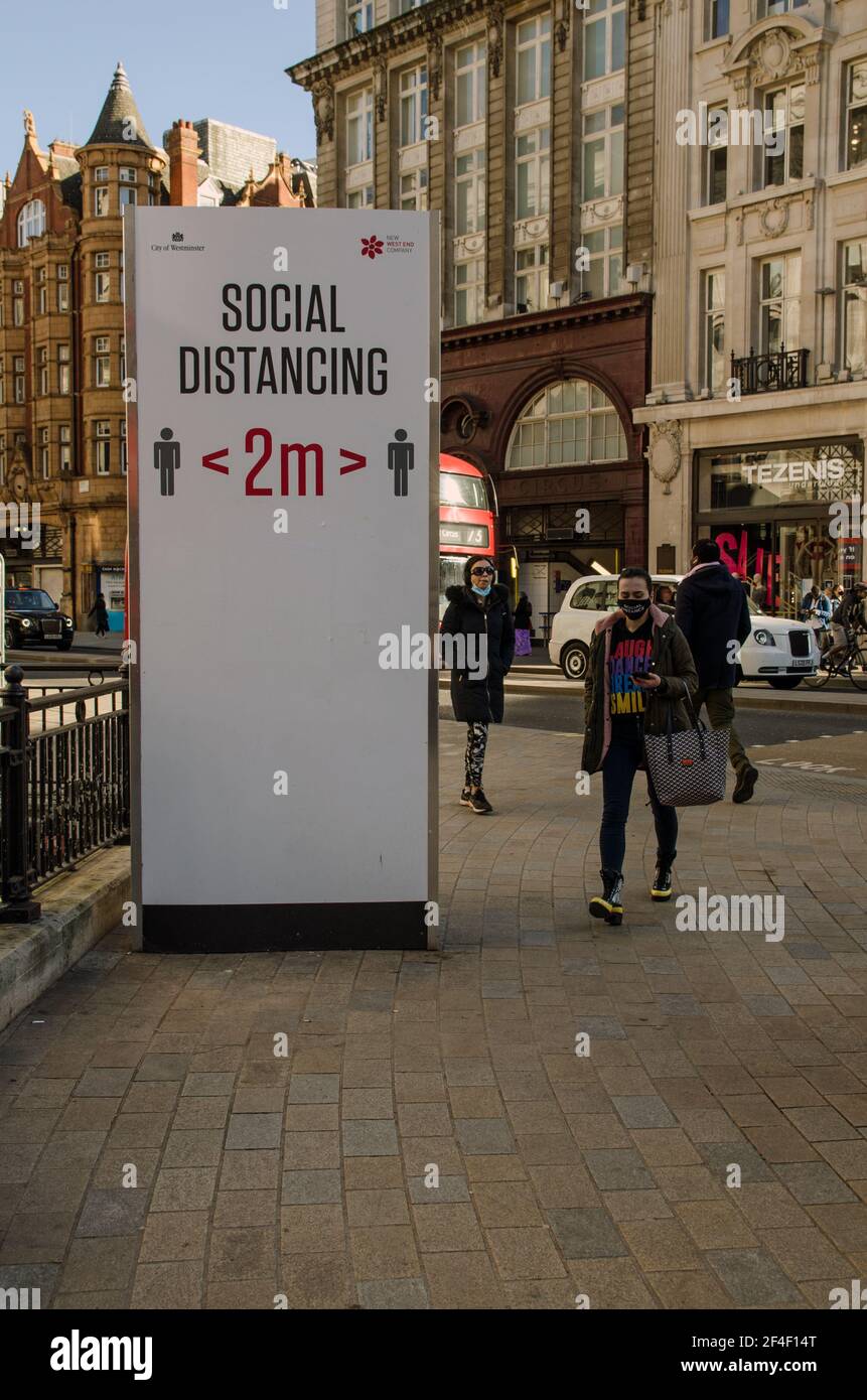 London, Großbritannien - 26. Februar 2021: Ein großes Schild, das Fußgänger ermutigt, sich im normalerweise geschäftigen Oxford Circus im Zentrum Londons auseinander zu halten. Viele Menschen Stockfoto