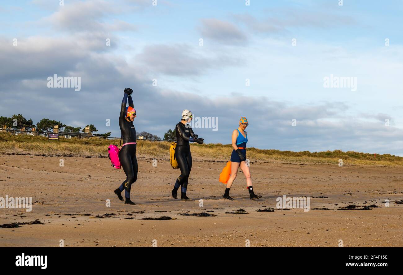 North Berwick, East Lothian, Schottland, Großbritannien, 21st. März 2021. UK Wetter: Wildschwimmer gehen im Firth of Forth im Freiwasser schwimmen. Wildbaden ist ein beliebter Sport für Einheimische in der Küstenstadt geworden. Diese Frauen sind einige der Stammgäste, die in den Sport jede Woche während des ganzen Jahres teilnehmen. Im Bild: Sarah, Jo und Alison schwimmen jede Woche, manchmal öfter in West Bay, während sie sich darauf vorbereiten, vom Strand aus mit Neoprenanzügen und Schwimmern ins Meer zu gehen Stockfoto