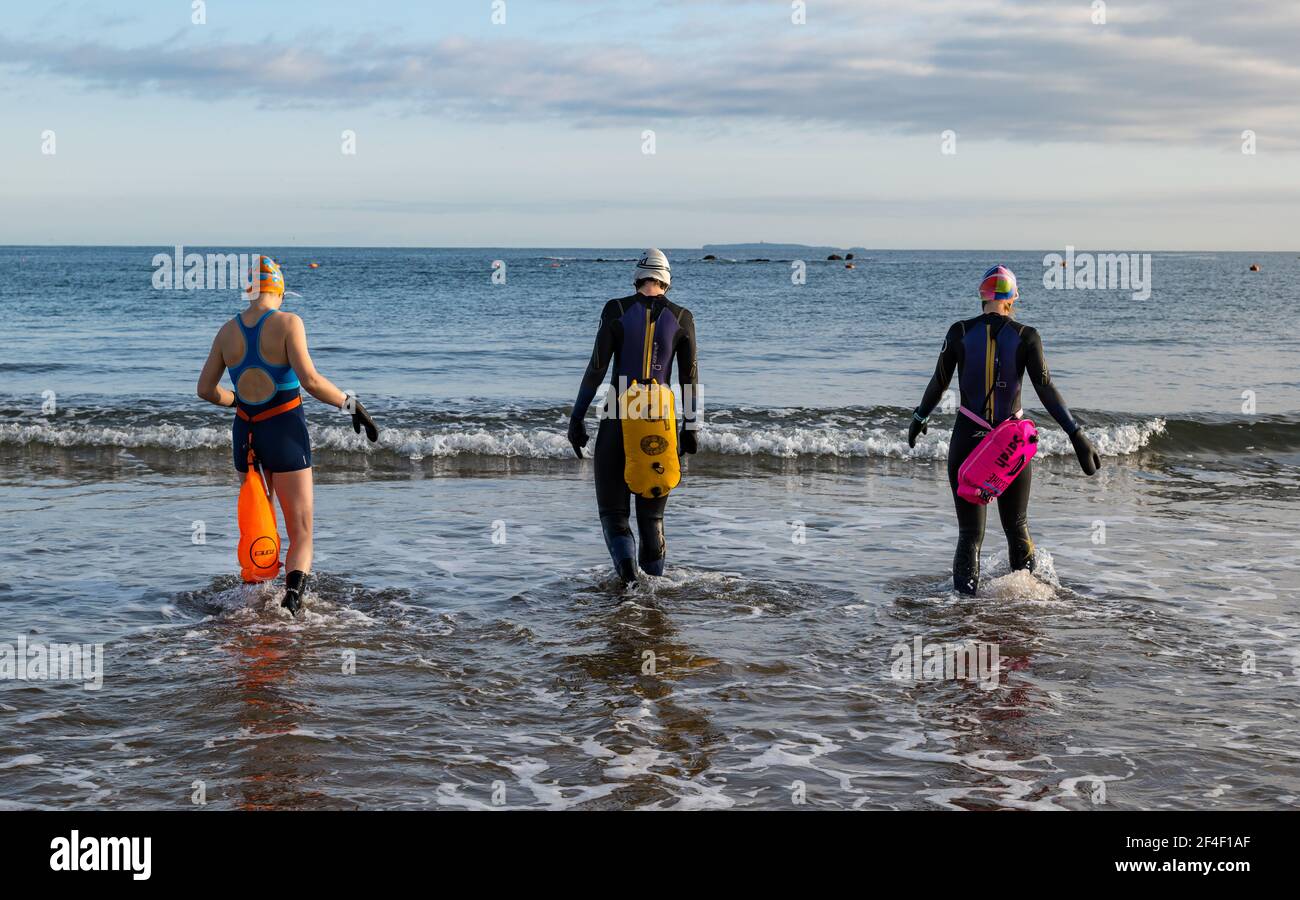 North Berwick, East Lothian, Schottland, Großbritannien, 21st. März 2021. UK Wetter: Wildschwimmer gehen im Firth of Forth im Freiwasser schwimmen. Wildbaden ist ein beliebter Sport für Einheimische in der Küstenstadt geworden. Diese Frauen sind einige der Stammgäste, die in den Sport jede Woche während des ganzen Jahres teilnehmen. Im Bild: Alison, Jo und Sarah schwimmen jede Woche, manchmal öfter in West Bay, als sie in Neoprenanzügen und Schwimmern ins Meer kommen Stockfoto