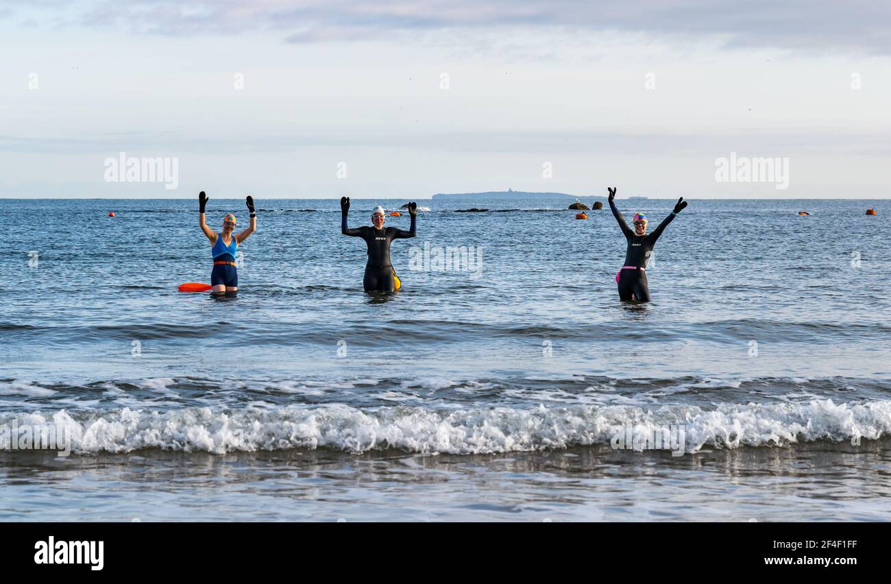 North Berwick, East Lothian, Schottland, Großbritannien, 21st. März 2021. UK Wetter: Wildschwimmer gehen im Firth of Forth im Freiwasser schwimmen. Wildbaden ist ein beliebter Sport für Einheimische in der Küstenstadt geworden. Diese Frauen sind einige der Stammgäste, die in den Sport jede Woche während des ganzen Jahres teilnehmen. Im Bild: Alison, Jo und Sarah schwimmen jede Woche, manchmal öfter in West Bay, als sie in Neoprenanzügen und Schwimmern ins Meer kommen Stockfoto