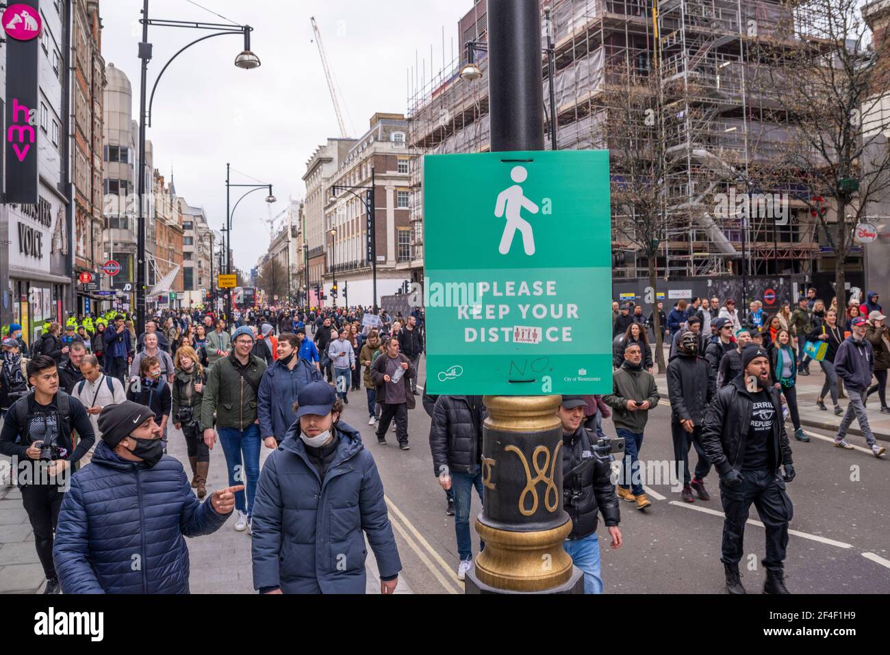 Demonstranten bei einem COVID 19 Anti-Lockdown-protestmarsch in Westminster, London, Großbritannien, vorbei an einem sozialen Distanzierungszeichen, das verändert wurde. Vandalisiert Stockfoto