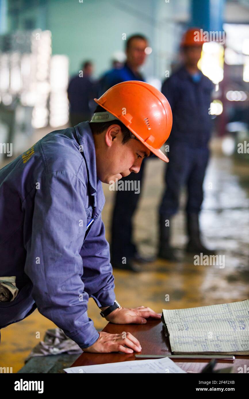 Pavlodar, Kasachstan - Mai 29 2012: Aluminium-Draht-und Kabel-Anlage. Betreiber Arbeiter in orange Hardhat lesen Sie ein Logbuch. Stockfoto
