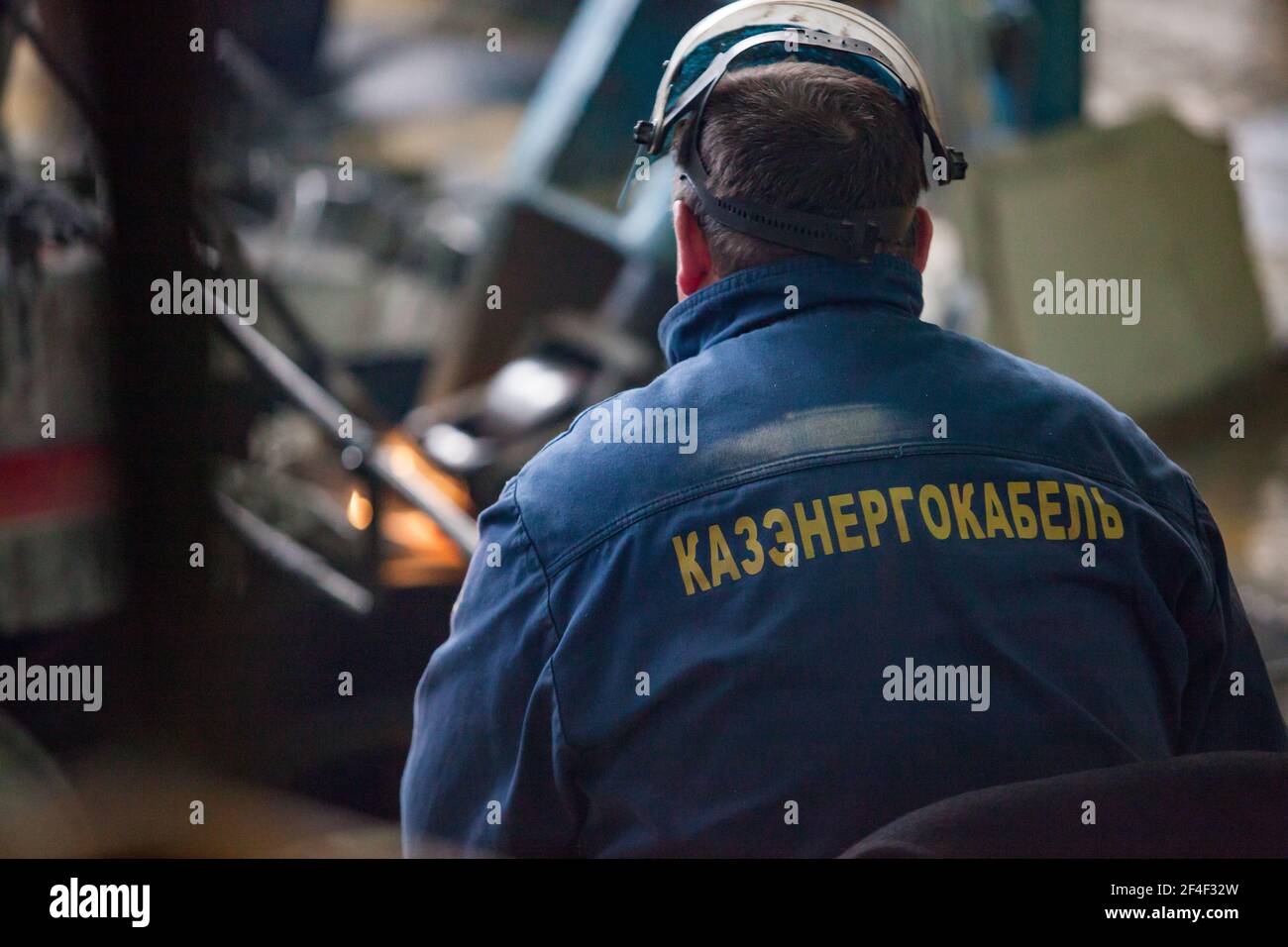 Pavlodar, Kasachstan - Mai 29 2012: Aluminium-Draht-und Kabel-Anlage. Bediener Arbeiter und verschwommene Schmelzmaschine. Konzentrieren Sie sich auf das Logo auf der Jacke. Stockfoto