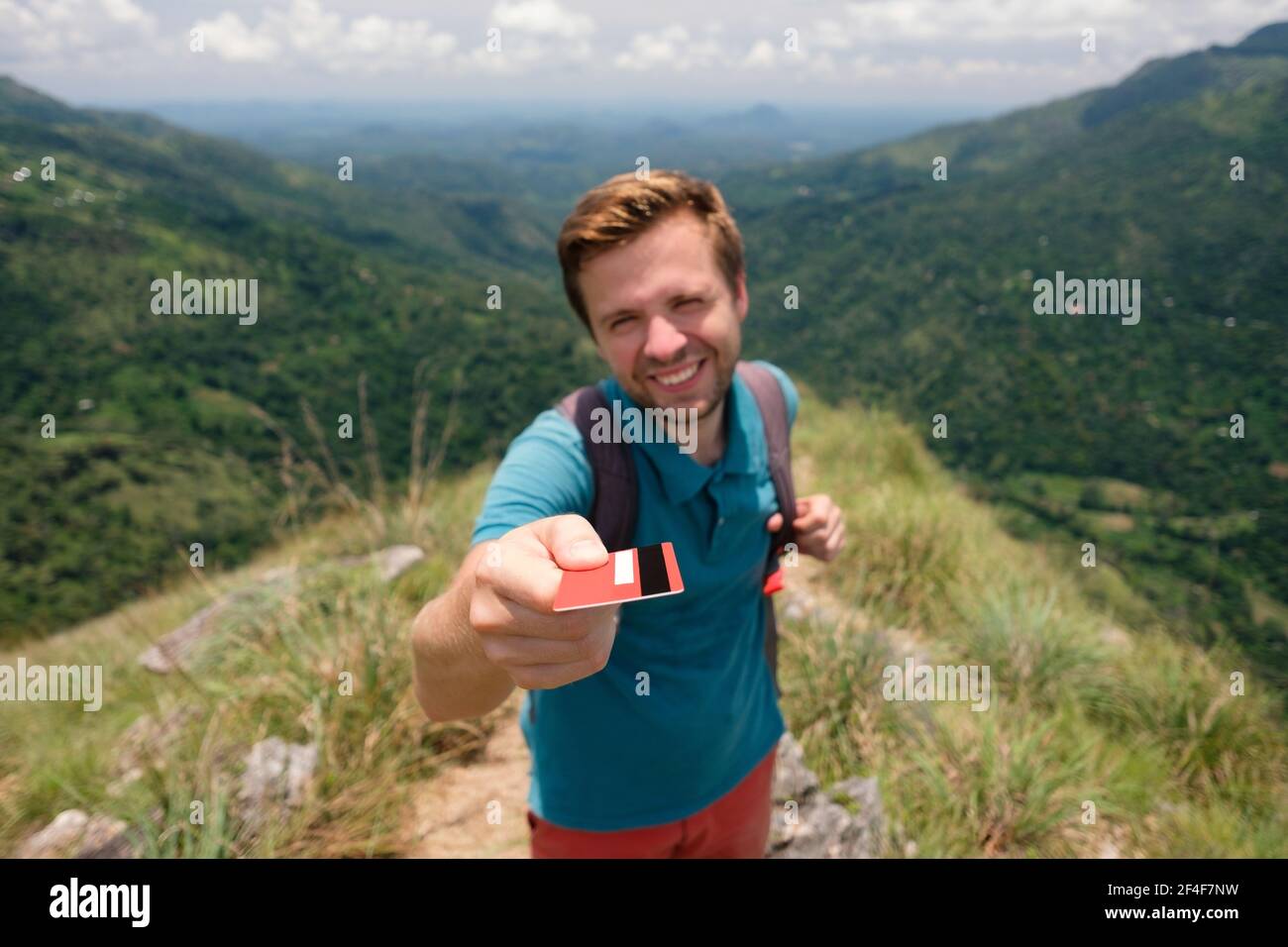 Junge lächelnde Mann zeigt leere Kreditkarte. Er steht an der Spitze des Berges und zeigt die outdoor Schönheit. Konzept der einfach Reisen Stockfoto