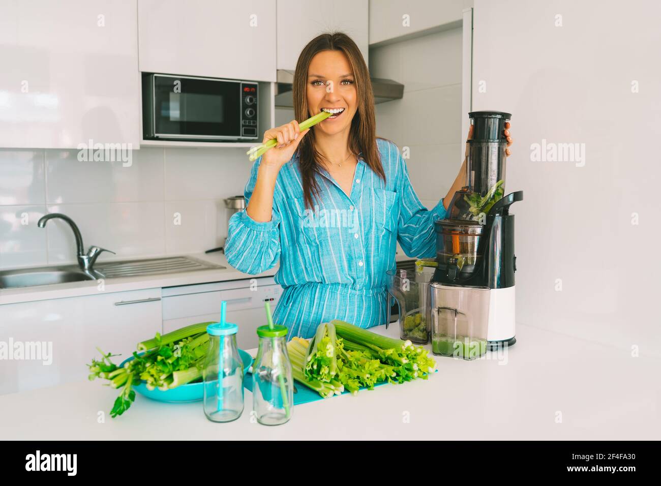 Frau, die frisch gepressten Selleriesaft in der Saftpresse macht Zuhause in der Küche Stockfoto