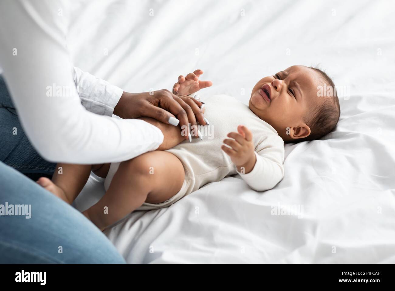 Schwarze Mutter tut Bauchmassage für weinende Säugling Stockfoto