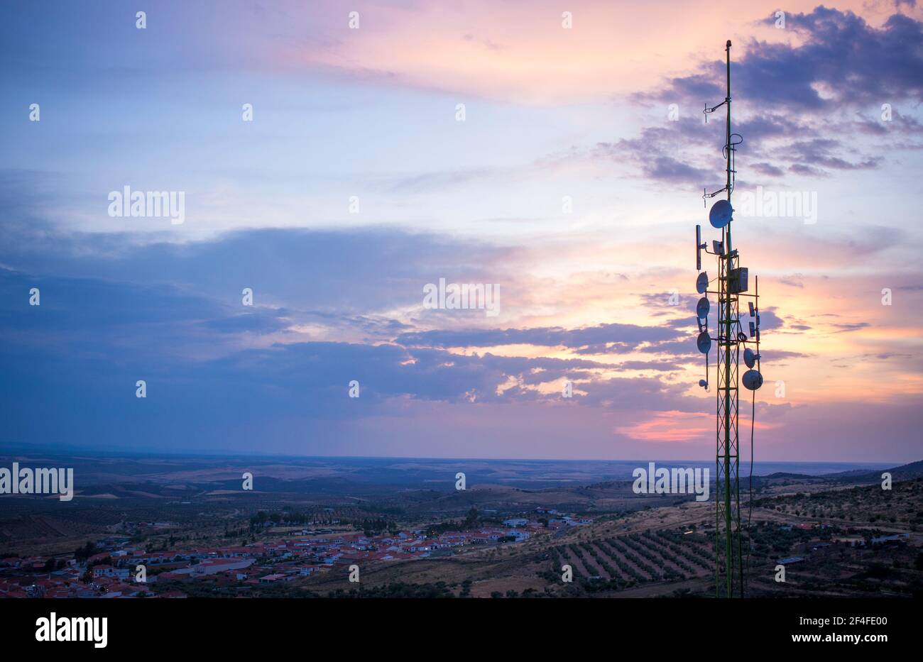 Sendestation Antennen auf dem Hügel der über kleinen Stadt. Ländliche Landschaft bei Sonnenuntergang Stockfoto