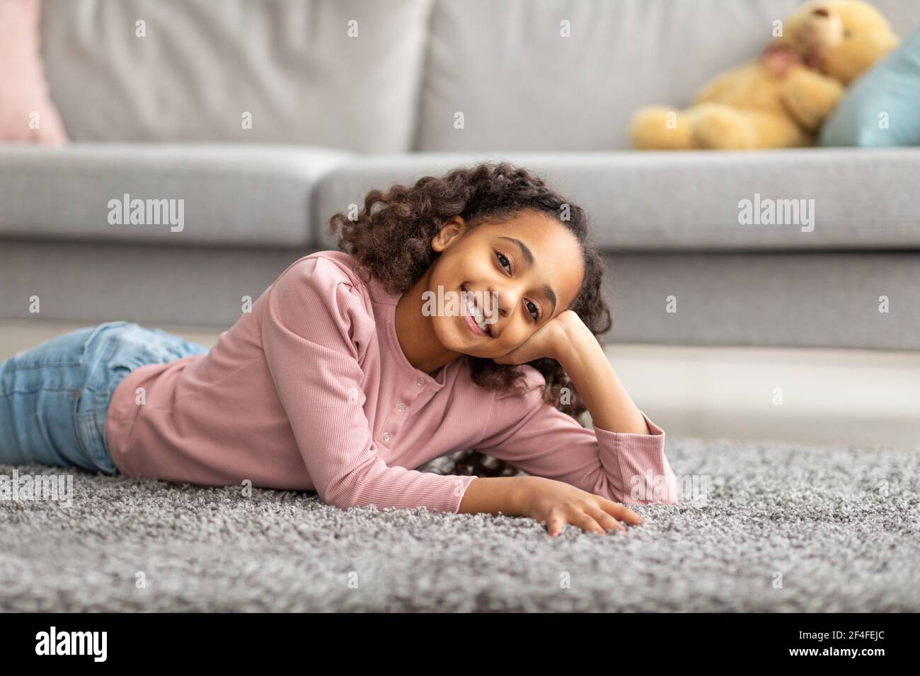 Teenager-Porträt. Positive afroamerikanische Mädchen lächelt vor der Kamera, lag auf dem Teppich zu Hause Stockfoto