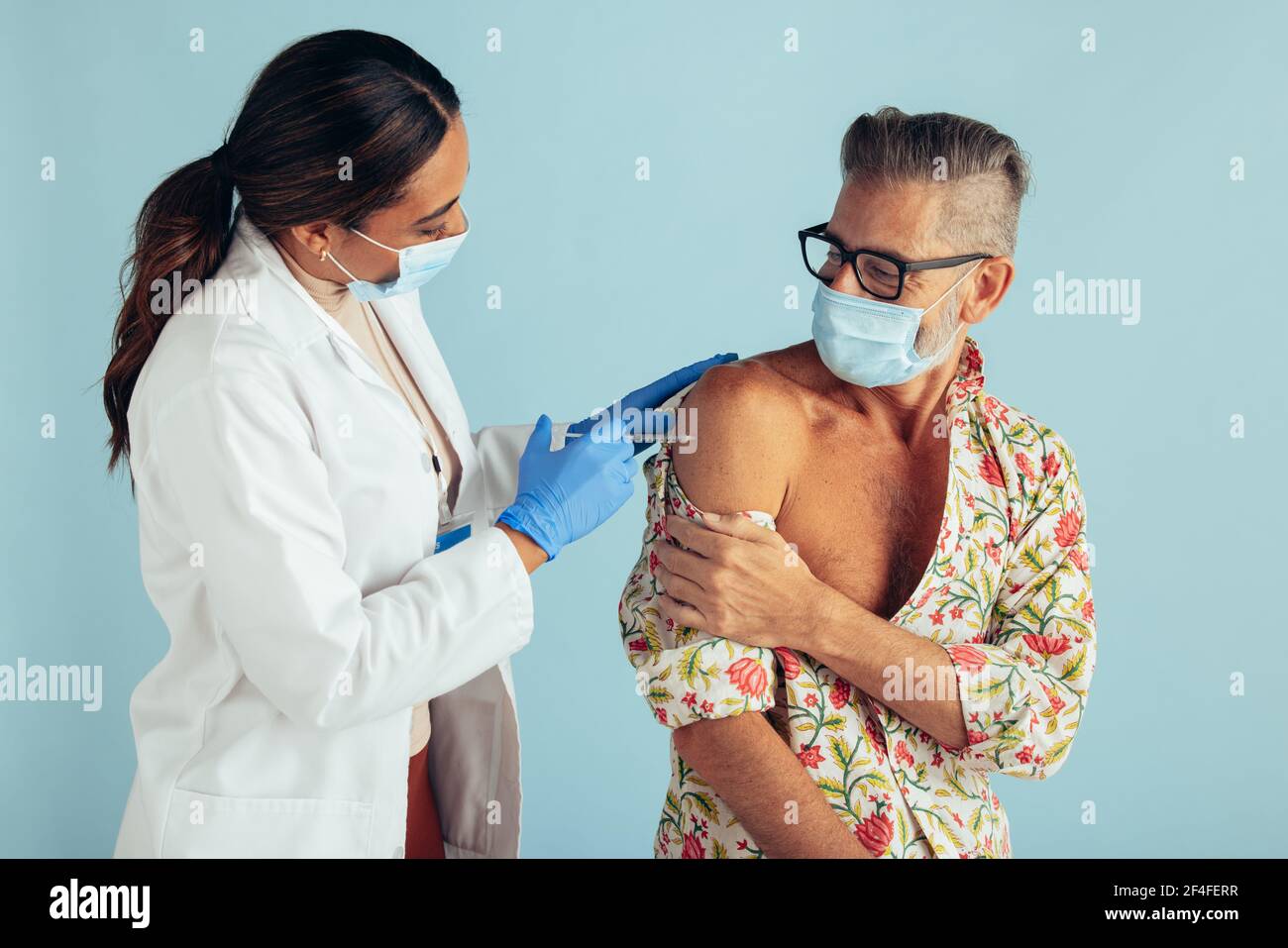 Ärztin gibt Coronavirus-Impfstoff an reifen Mann. Arzt und mittelalter Mann, der während der covid-19-Impfung Schutzmasken trägt Stockfoto