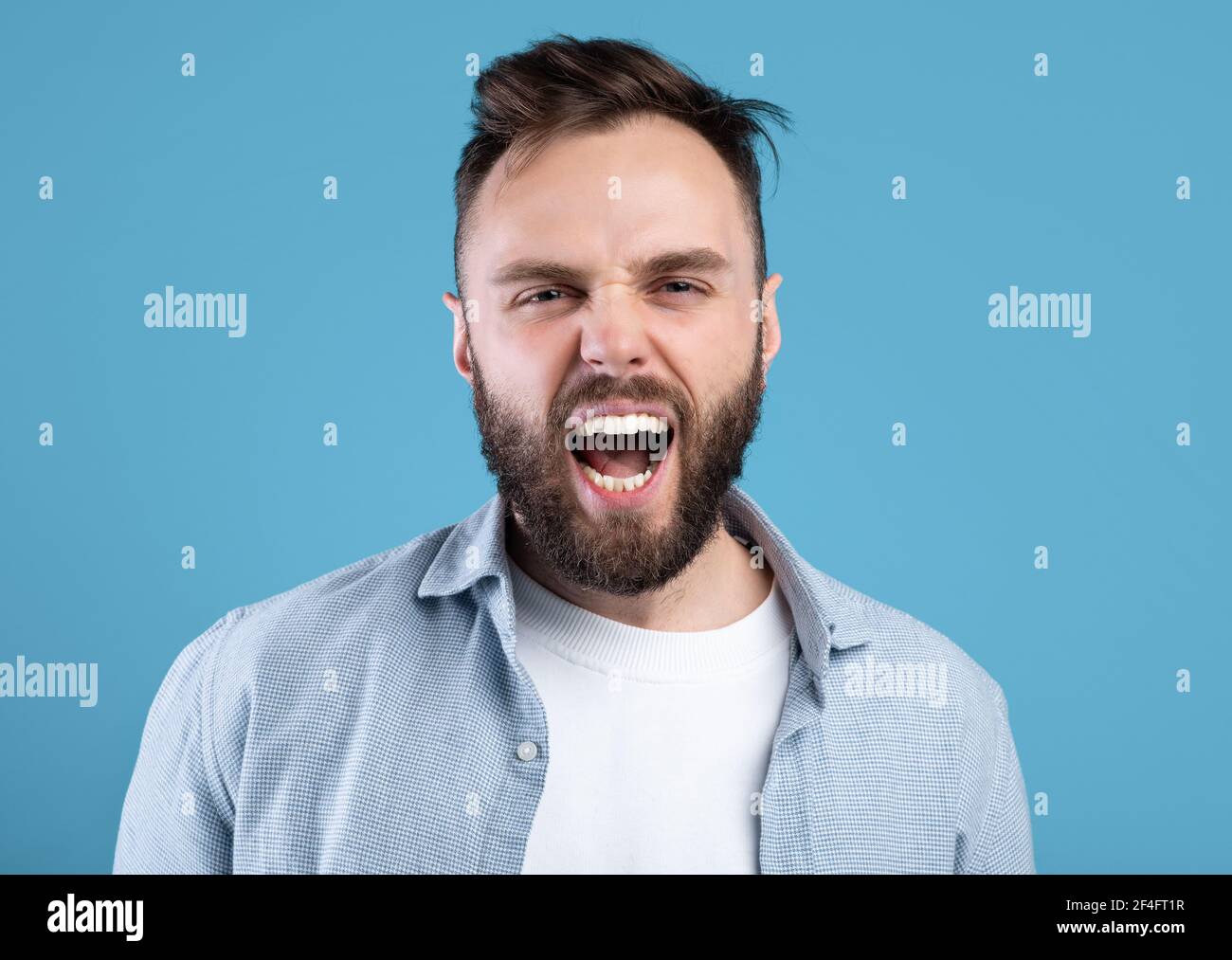 Wütend bärtigen Kerl schreien vor Wut, drückt seine Aggression über blauen Studio-Hintergrund Stockfoto