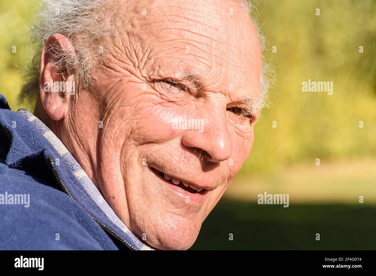 Porträt eines lächelnden älteren Mannes im Garten bei sonnigem Tag. Stockfoto