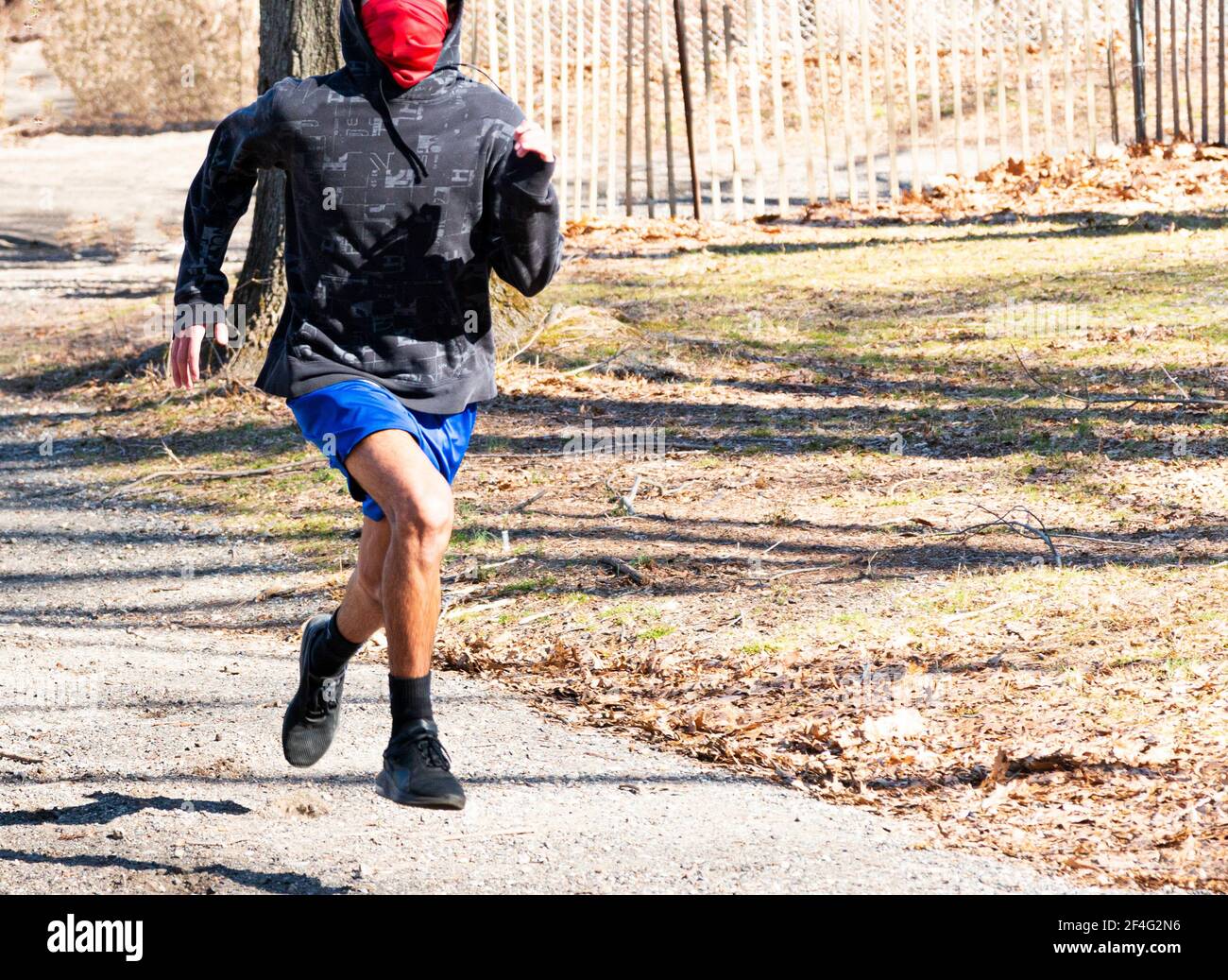 Ein Gymnasiast läuft in einem Park mit einer roten Gamasche über dem Mund, um sich vor COVID-19 zu schützen. Stockfoto