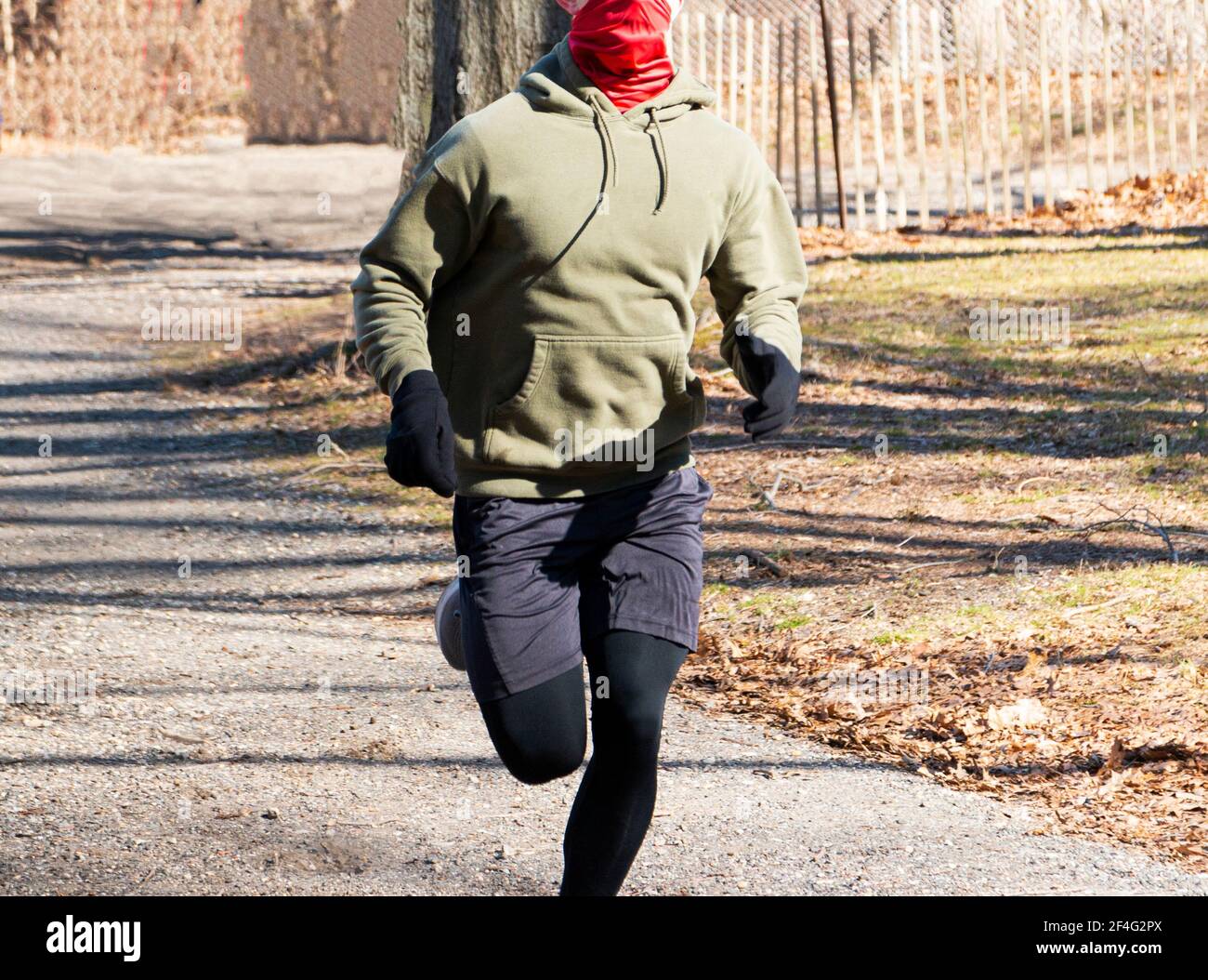 Ein Läufer läuft auf einem Waldweg mit einem roten Gamaschen über seinem Gesicht, um sich vor der COVID-19-Infektion des Coronavirus zu schützen. Stockfoto