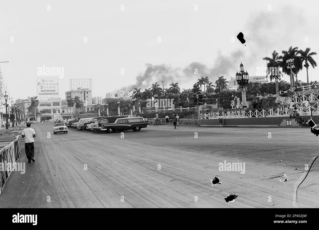 Breite Aufnahme von Fußgängern und Autos auf einem breiten Feldweg neben einem großen Park in der Innenstadt von Havanna, Kuba, 1964. Aus der Sammlung Deena Stryker Photographs. () Stockfoto