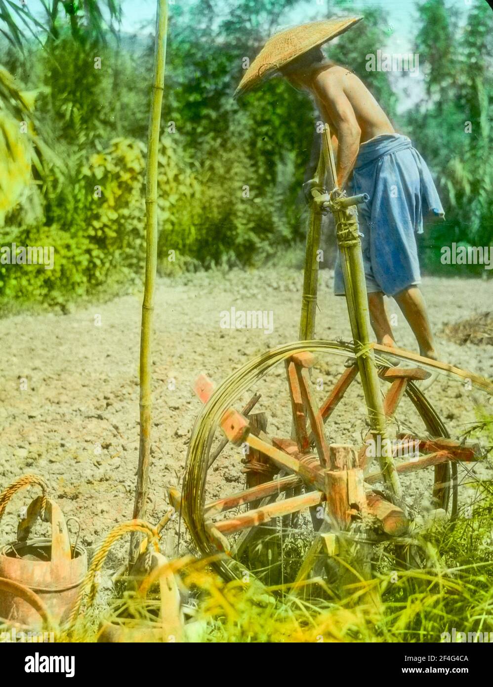 Ein männlicher Bauer, im Profil, geht auf einem manuellen Wasserrad, um ein Felsenfeld an einem sonnigen Tag zu bewässern, Sichuan, China, 1917. Aus der Sammlung Sidney D. Gamble Photographs. () Stockfoto