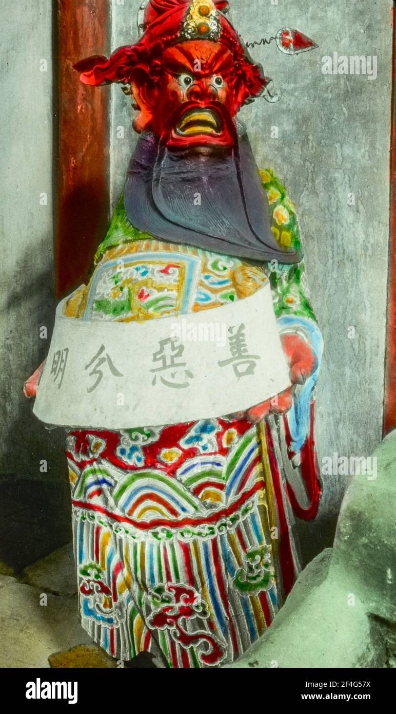 Eine Skulptur eines Richters, mit roter Haut, einem langen schwarzen Bart und bunten Kleidern, mit einem Schild mit chinesischem Text, Sichuan, China, 1917. Aus der Sammlung Sidney D. Gamble Photographs. () Stockfoto