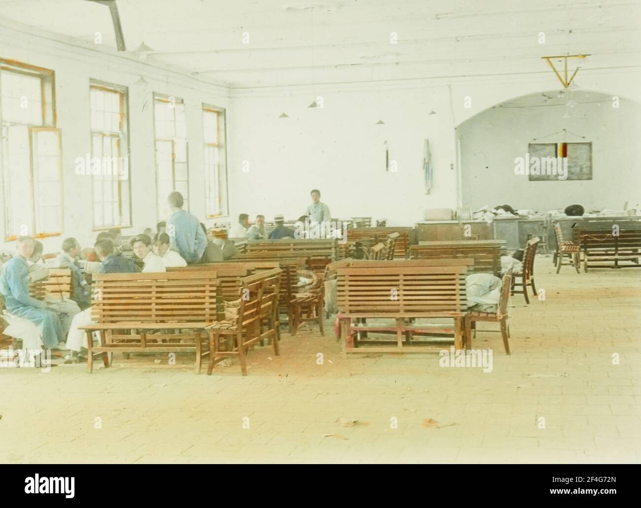 Eine Gruppe von Studenten, die wegen Protesten im Zusammenhang mit der Bewegung vom 4. Mai inhaftiert sind, sitzen und stehen auf hölzernen Lattenbänken, die in der Nähe von sonnigen Fenstern in einer großen Halle, Peking, China, 1919, platziert sind. Aus der Sammlung Sidney D. Gamble Photographs. () Stockfoto