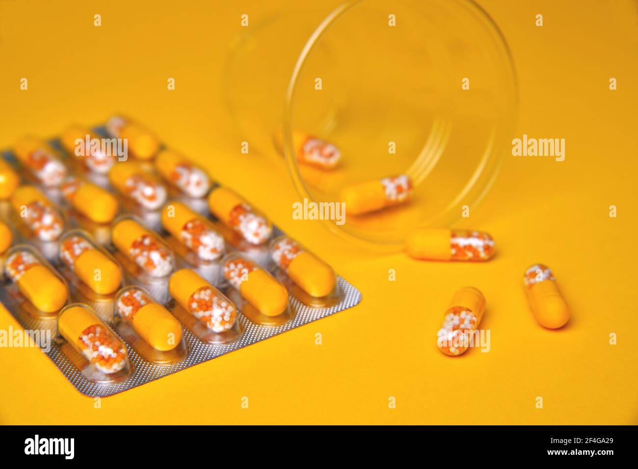 Kapseln in einer Blister und einem Glas. Medizinische Tabletten, Vitamine in einem Granulat, in gelben Kapseln auf einem gelben Hintergrund. Blur als kreative Idee der A Stockfoto