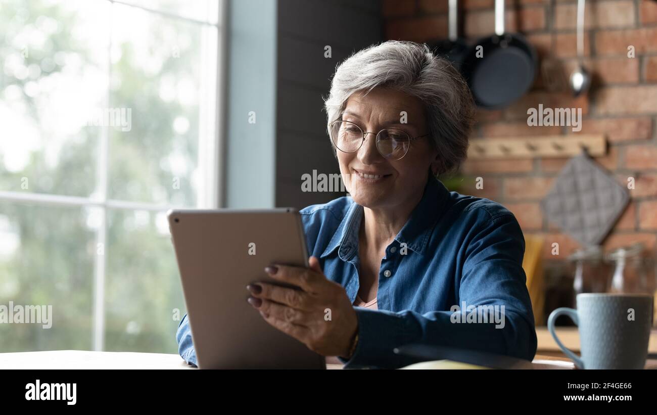 Positive ältere hispanische Oma zu Hause entspannen Tablet-Gerät verwenden Stockfoto