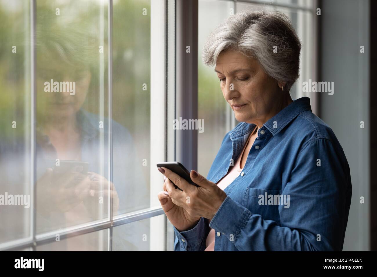 Seriöse lateinische Rentnerin steht für eine SMS per Zelle Stockfoto