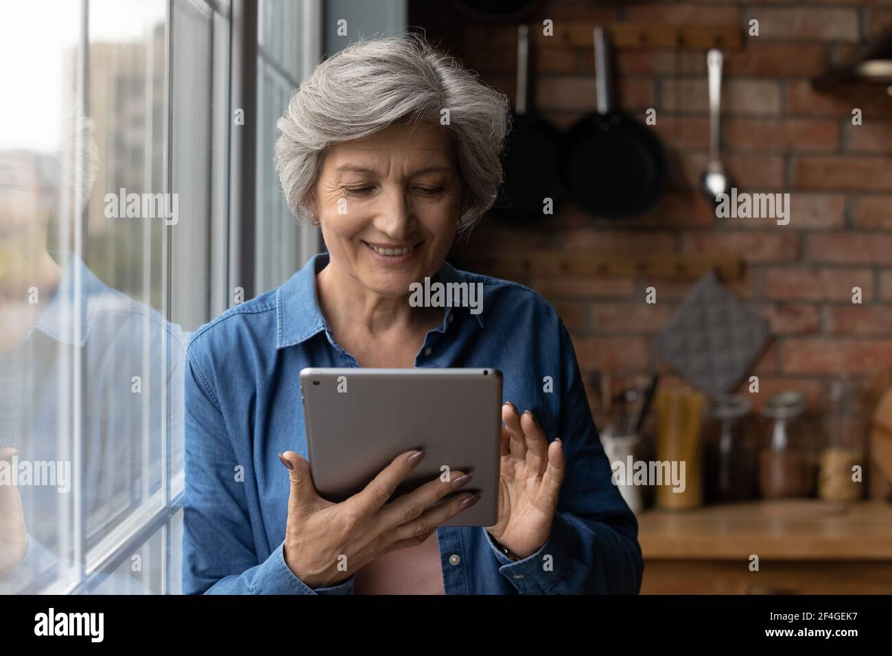 Lächelnde lateinische Frau mittleren Alters verwenden Tablet-Computer in der Küche Stockfoto