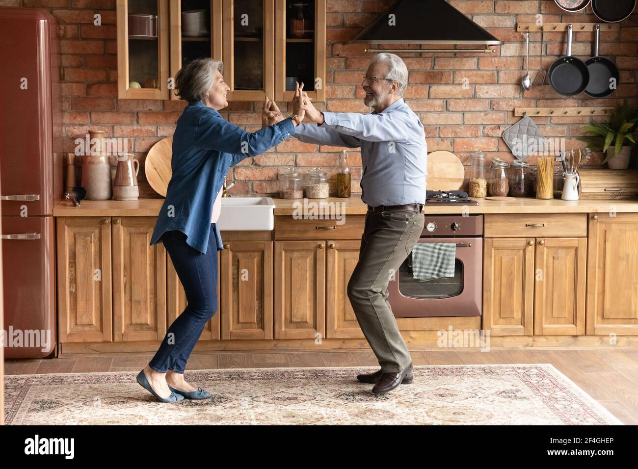 Aktives Familienpaar im Alter, das in der modernen Holzküche tanzt Stockfoto
