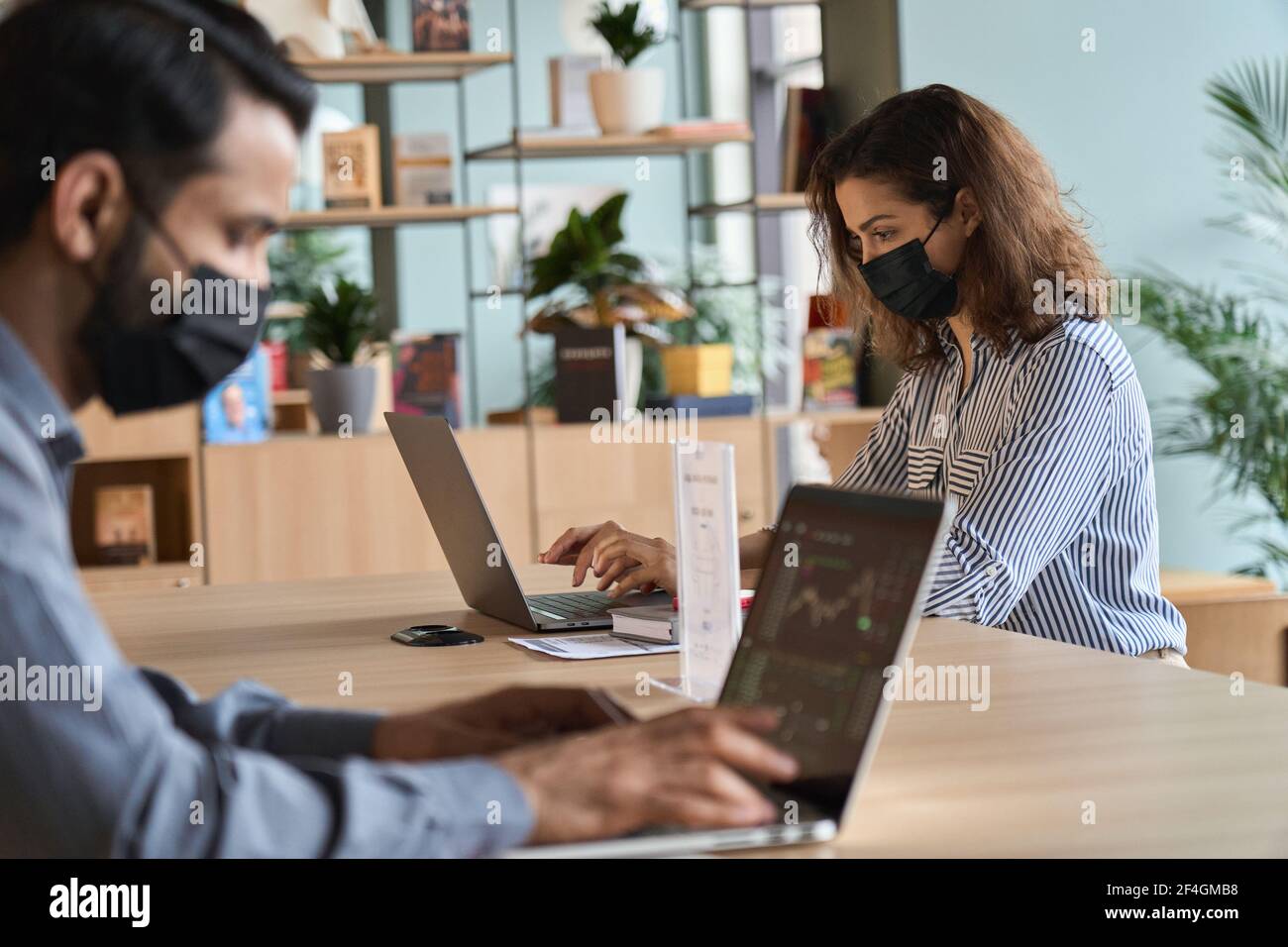 Junge lateinische Frau trägt Gesichtsmaske arbeiten auf Laptop sicheren Abstand zu halten. Stockfoto