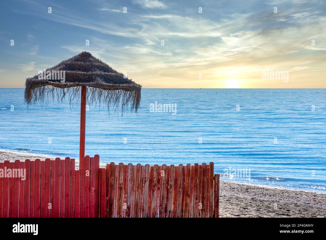 Sonnenuntergang am Strand von Nerja (Spanien) mit Sonnenschirm Und ein roter Holzzaun am Ufer des Ruhiges Mittelmeer Stockfoto