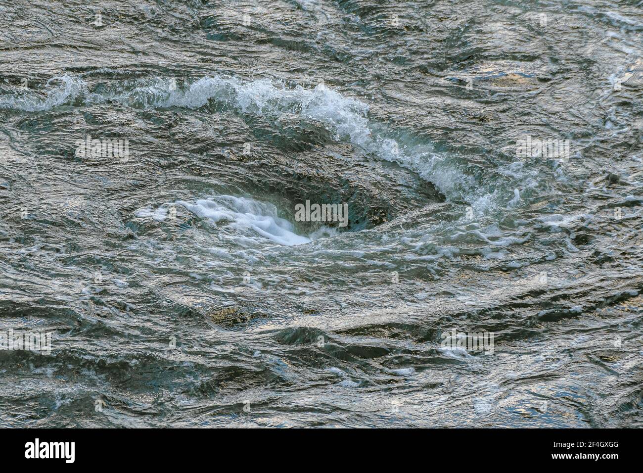 Ein kleiner, aber turbulenter Whirlpool bildete sich dort, wo ein Fluss auf einen Hafen trifft. Viel Spray und Schaum im dunkelgrün gefärbten Wasser. Stockfoto