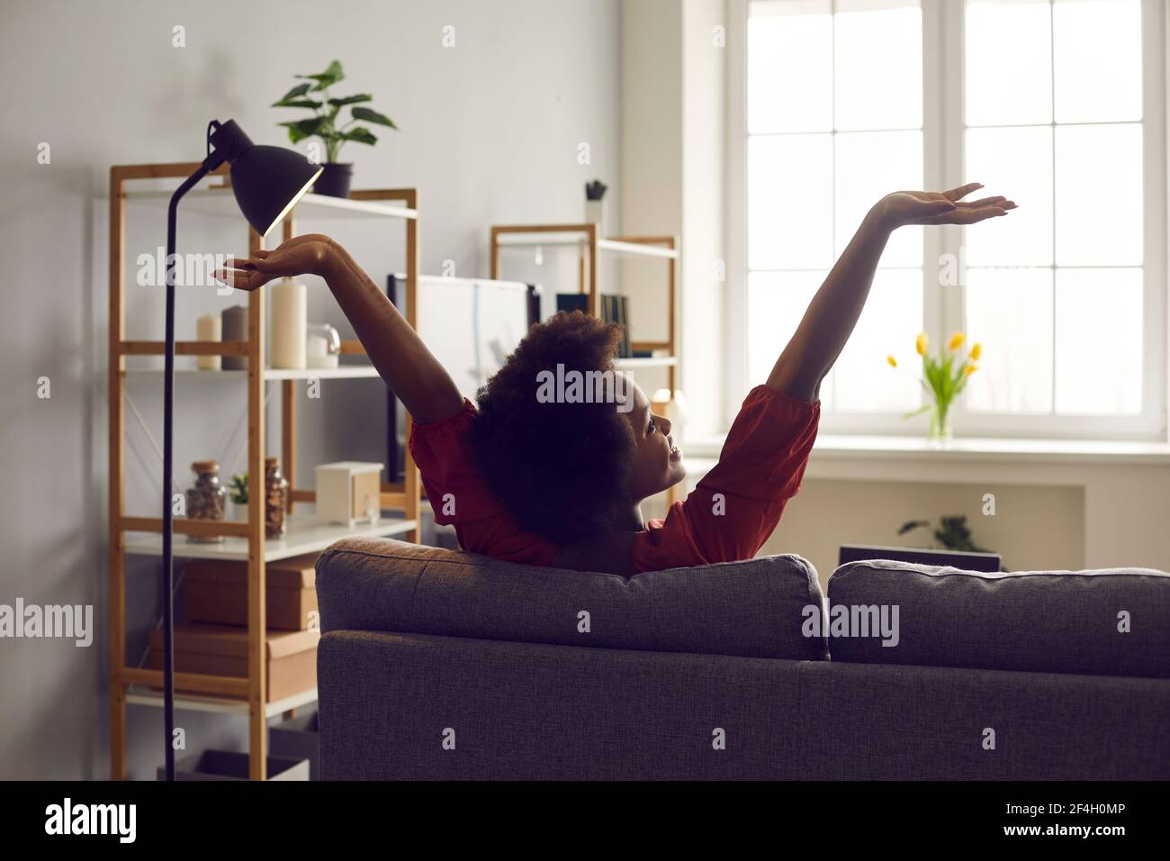 Rückansicht einer glücklichen jungen Frau, die ihre Arme im Sitzen streckt Auf der Couch im Wohnzimmer Stockfoto