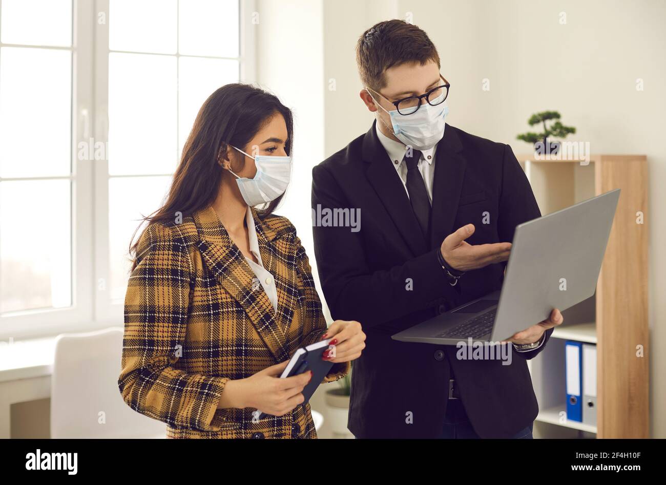 Büroangestellte in medizinischen Gesichtsmasken arbeiten an Business-Projekt Und mit Laptop Stockfoto