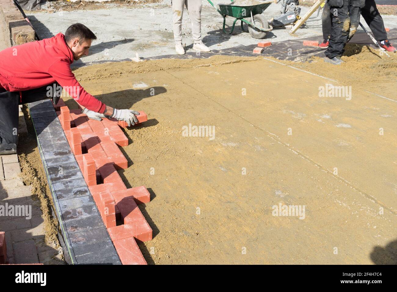 Fertiger legt erste Reihe von Pflastersteinen auf der Basis Sandschicht unter einem sonnigen Tag, England Stockfoto