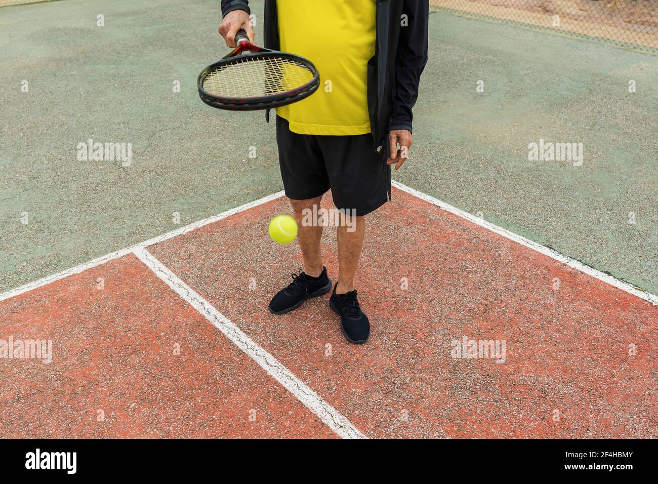 Crop Senior Sportler hüpfenden Ball auf Schläger während der Vorbereitung auf Tennismatch auf dem Platz Stockfoto