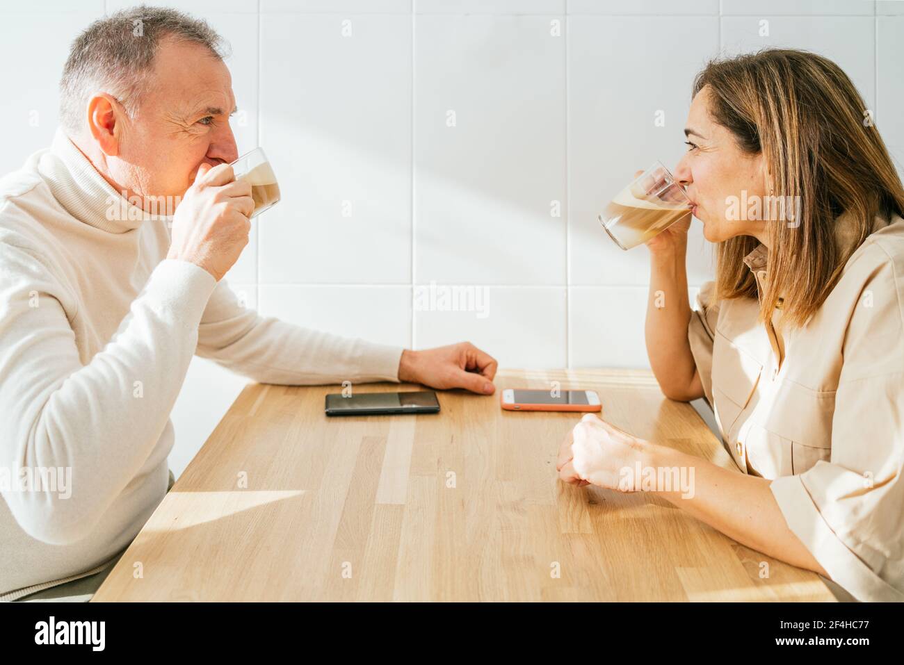 Seitenansicht des Inhalts Erwachsener Paar sitzt am Tisch in Küche und genießen aromatischen Kaffee beim Frühstück und suchen Aufeinander zu Stockfoto