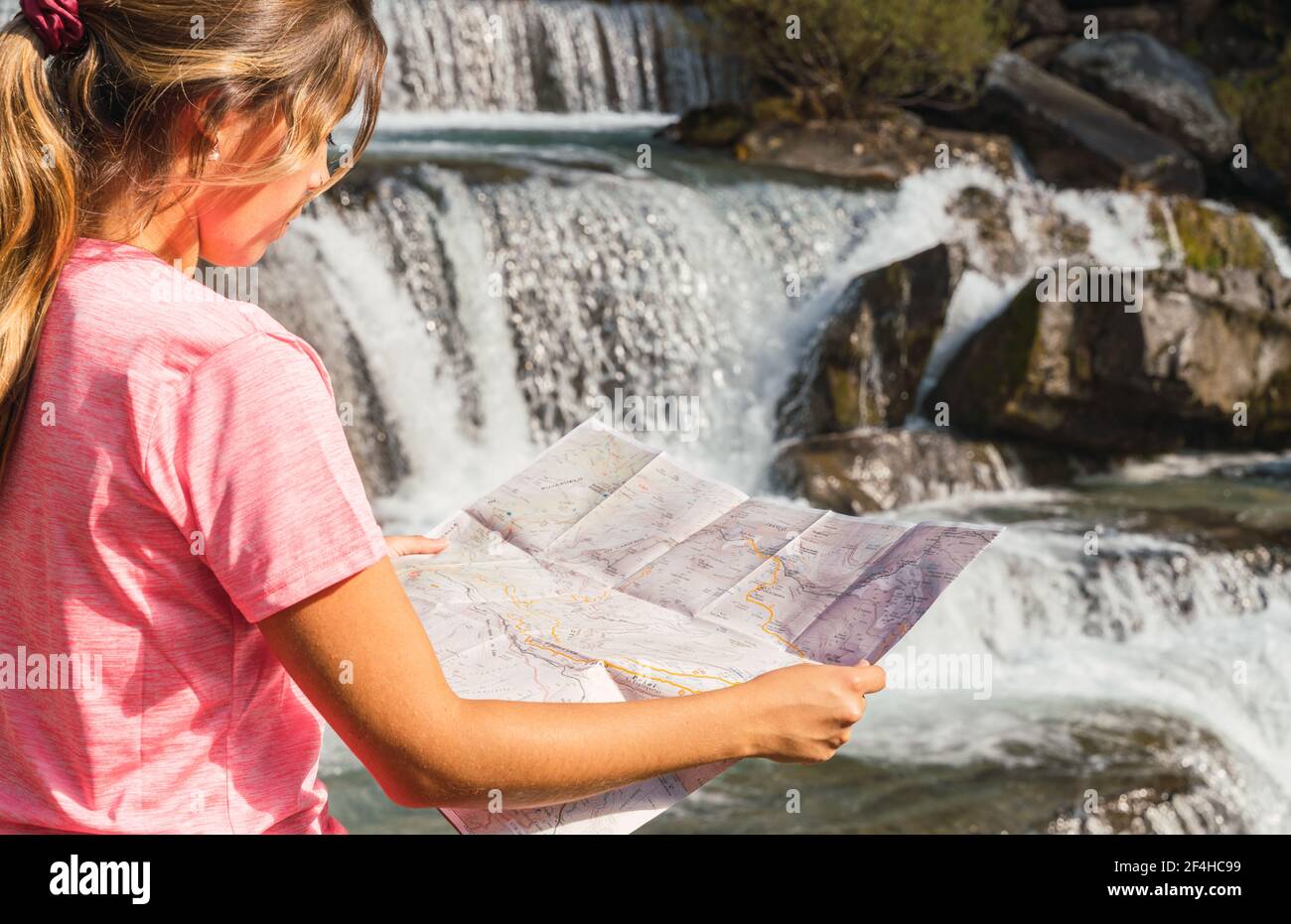 Seitenansicht einer Reisenden Frau, die mit einer Papierkarte in der Nähe des Wasserfalls im Nationalpark Ordesa y Monte Perdido steht und sich während des Urlaubs in den Pyrenäen orientiert Stockfoto