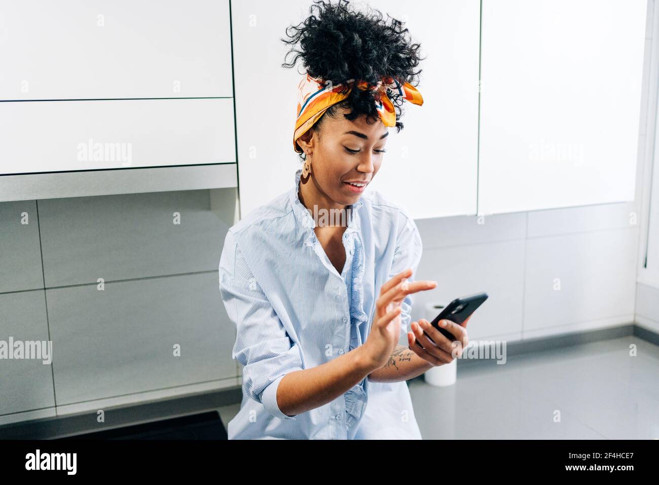 Afroamerikanische Frau, die auf dem Smartphone im Internet surft, während sie sich im Hotel aufmachen Arbeitsplatte in der Küche am Morgen Stockfoto