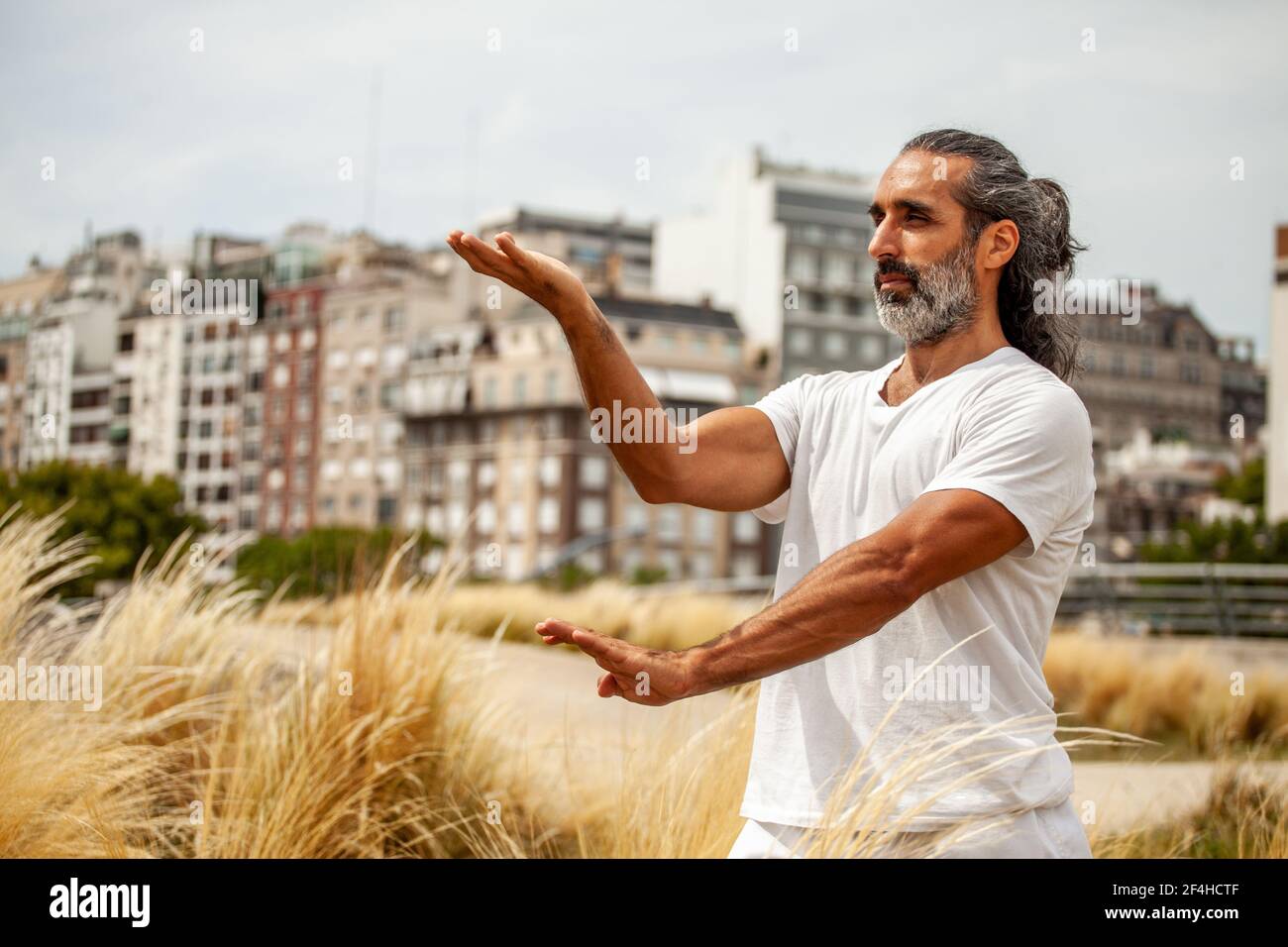 Reife unrasiert ethnischen männlich in weiß Outfit freuen sich, während Yoga gegen Stadtgebäude üben Stockfoto