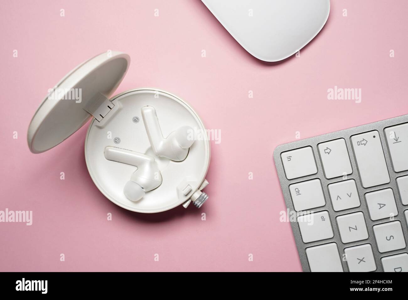 Zusammensetzung der weißen, schnurlosen Ohrhörer in der Draufsicht In der Nähe von Laptop-Tastatur und -Maus auf rosa Schreibtisch platziert Stockfoto