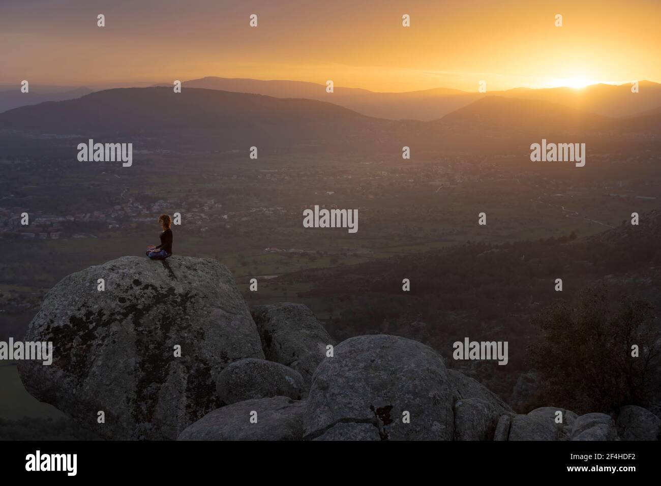 Werdende Frau in Zierkleid sitzt auf Yoga-Ball mit Kinderkleidung gegen Kommode im Zimmer Stockfoto