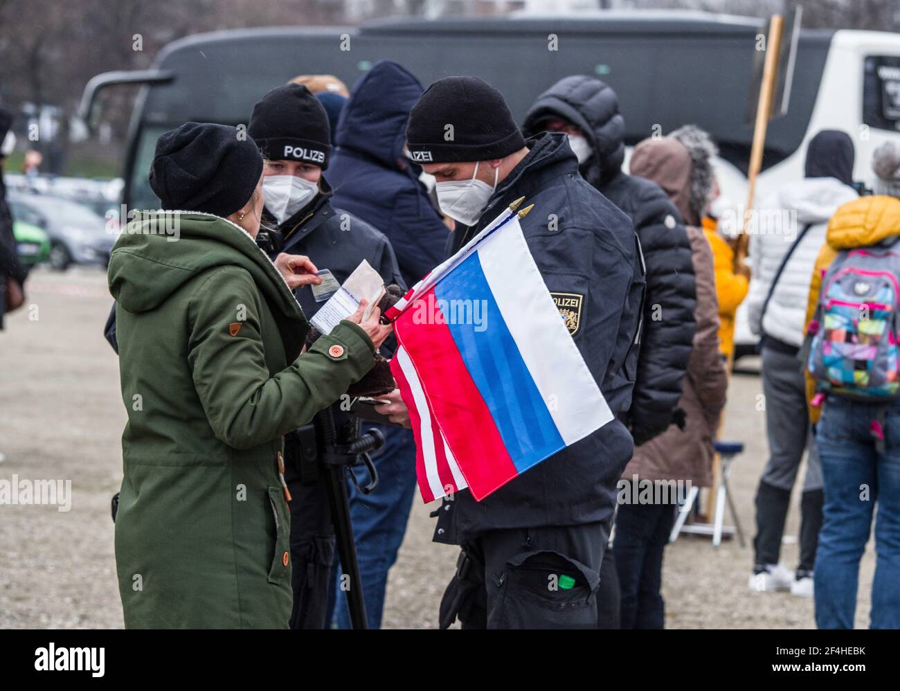 München, Bayern, Deutschland. März 2021, 21st. Eine entlarvte Frau mit russischer und amerikanischer Flagge wird bei der Demo der Gemeinschaft Zukunft von der Polizei kontrolliert. Die Gruppe Gemeinsame Zukunft unter der Leitung von Susanna Grill von Cocoon Hotels veranstaltete auf der Münchner Theresienwiese eine Demonstration, die ein Ende der Sperrungspolitik Deutschlands und vernünftige Anti-Corona-Maßnahmen forderte. Trotz der Forderungen, dass 1.000 "unantastbare Menschen" dort sein sollten, hatte die Gruppe weniger als 100, mit vielen bekannten Querdenken/Corona Rebel und Neonazi/NPD Mitgliedern, rechtsextremen/Verschwörungsmedien und Vertretern von Epoch Times/Falun Gong/N Stockfoto