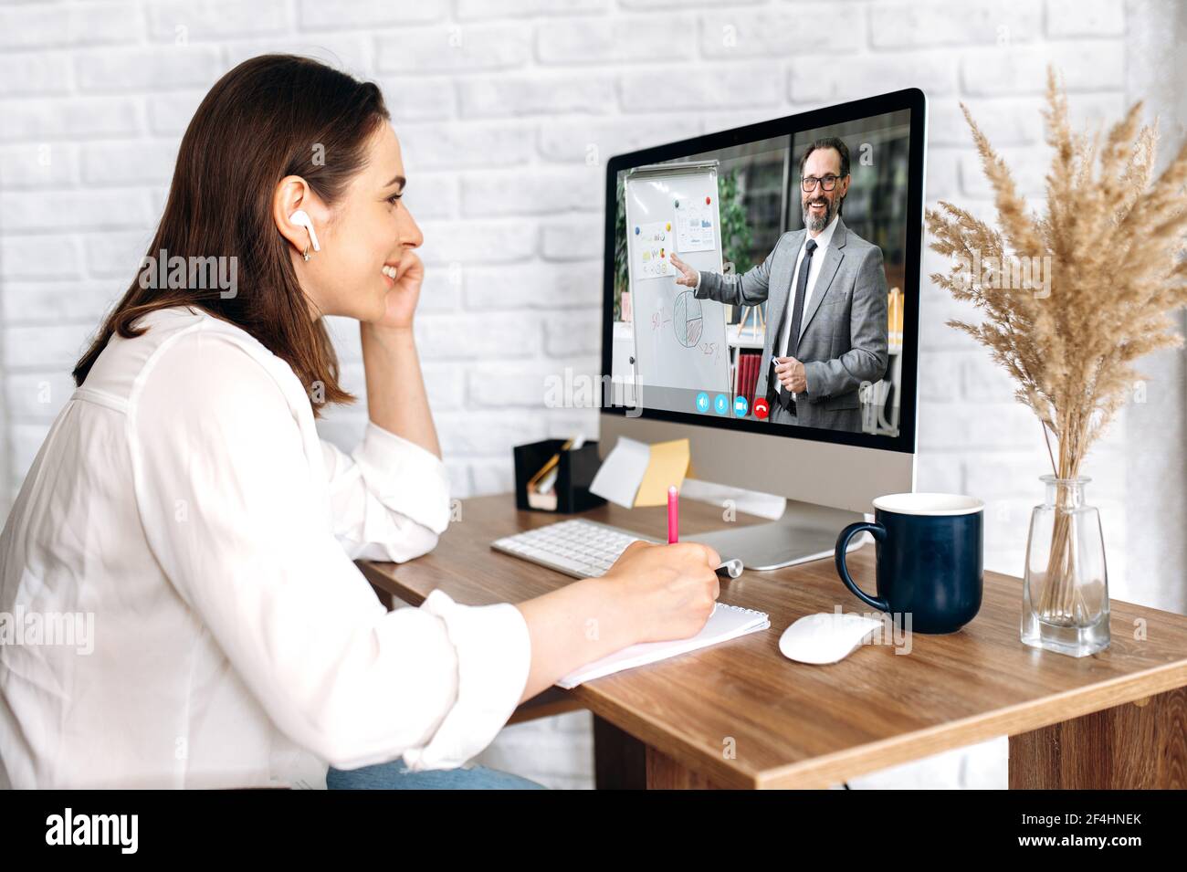 Online-Lernen. Videoanruf. Zufriedene junge Frau, aus der Ferne studieren, Notizen machen, auf dem Computer-Bildschirm männlichen Tutor führt eine Online-Lektion mit Informationen auf einem Flipchart, von zu Hause aus studieren Stockfoto